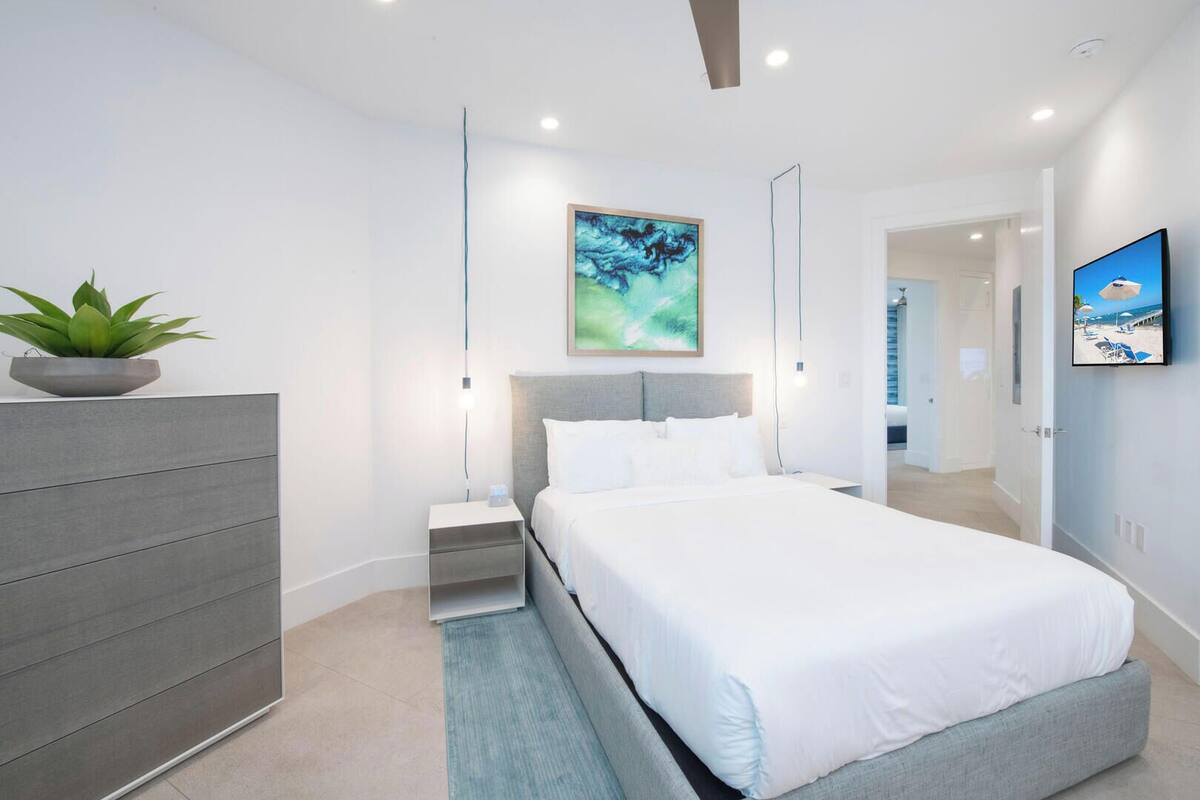 A modern bedroom with a bed, a nightstand, a dresser, a painting, and a TV.
