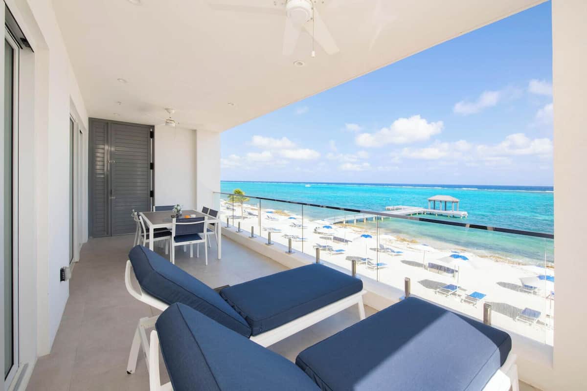 A balcony with a view of the ocean, a table, and two lounge chairs.