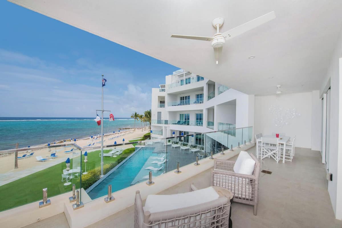 A balcony with a pool, lounge chairs, and a view of the ocean.