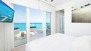 Une chambre d’hôtel moderne avec un grand lit, une télévision, un balcon donnant sur l’océan et un tableau au mur.