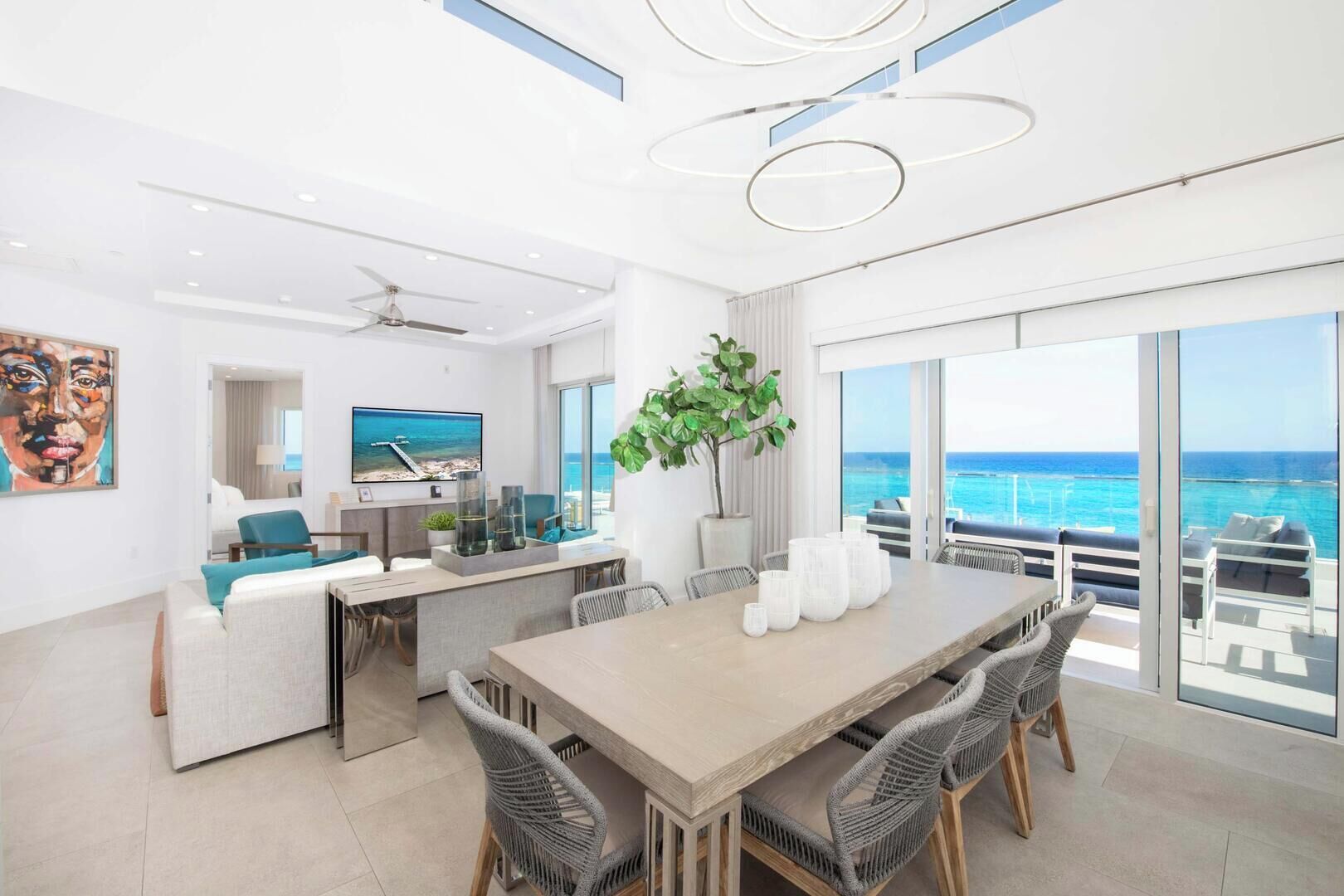 A modern hotel room with a large dining table, comfortable seating, a TV, and a view of the ocean.