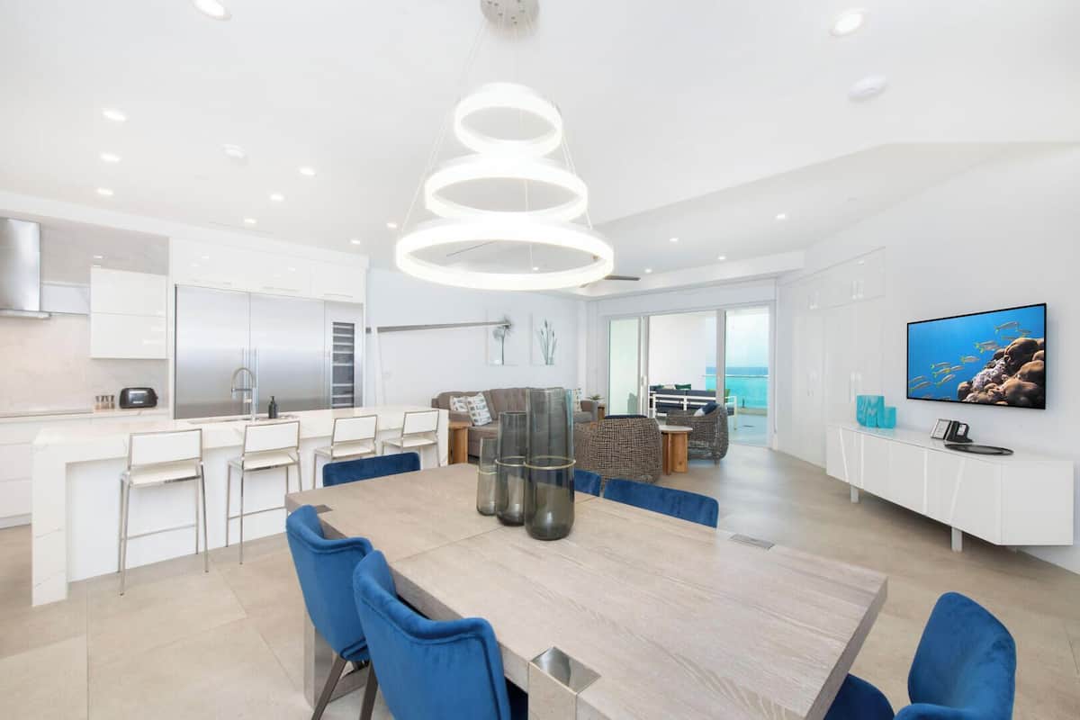 A modern kitchen with white cabinets, a stainless steel refrigerator, and a dining area with a wooden table and blue chairs.