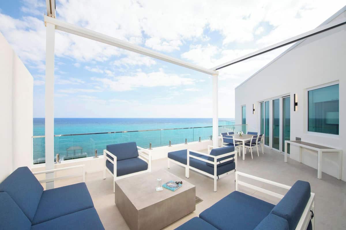A balcony with a view of the ocean, a table with chairs, and blue sofas.