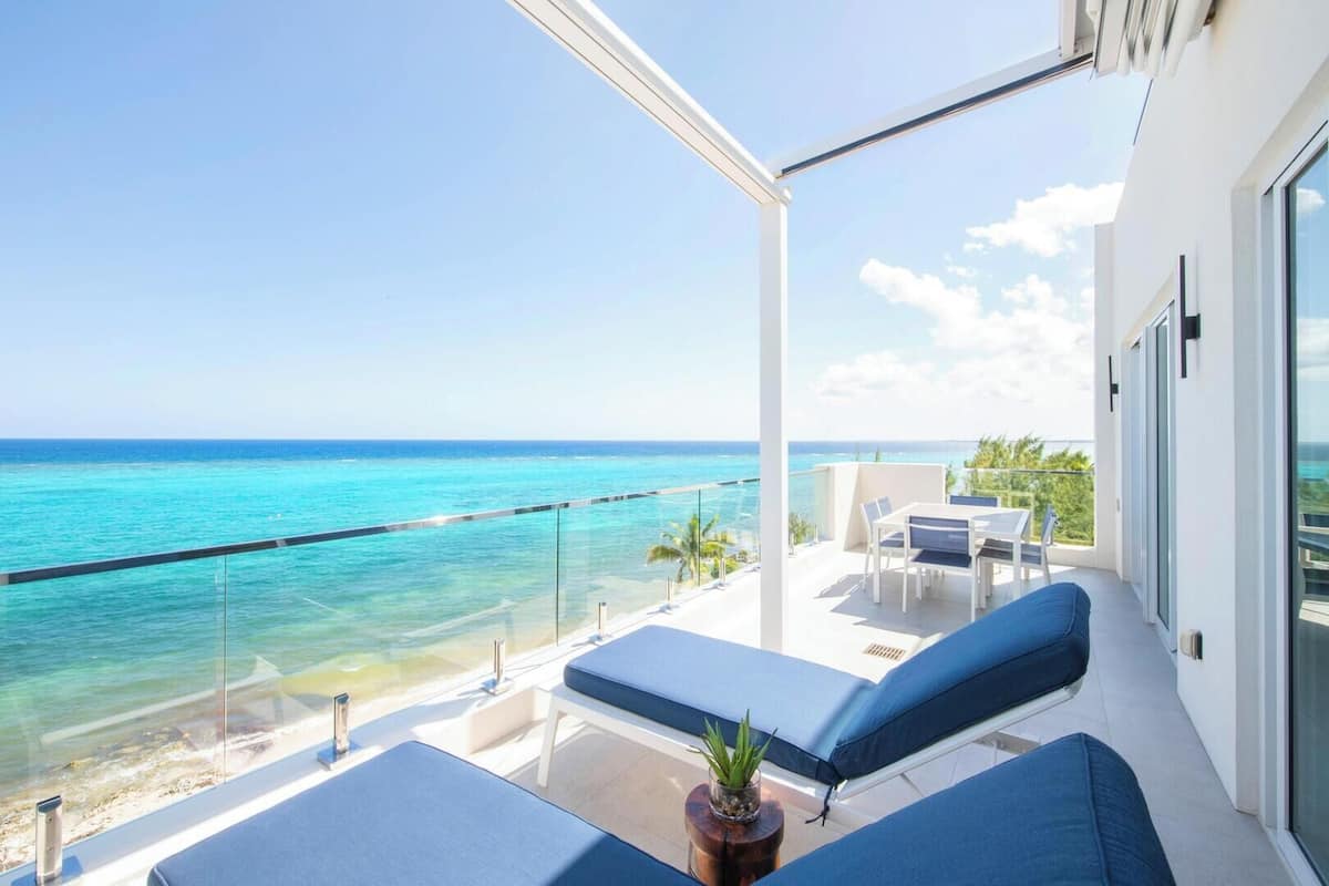 A balcony with a view of the ocean, a table with chairs, and a potted plant.