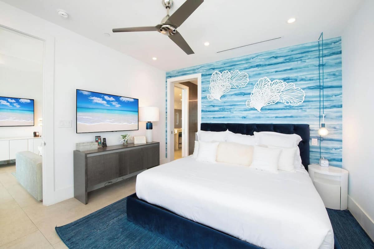 Un dormitorio moderno con una cama grande, un ventilador de techo, un televisor y una pared con un diseño abstracto azul.