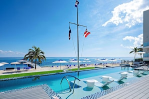 A poolside area with lounge chairs, umbrellas, and a view of the ocean.