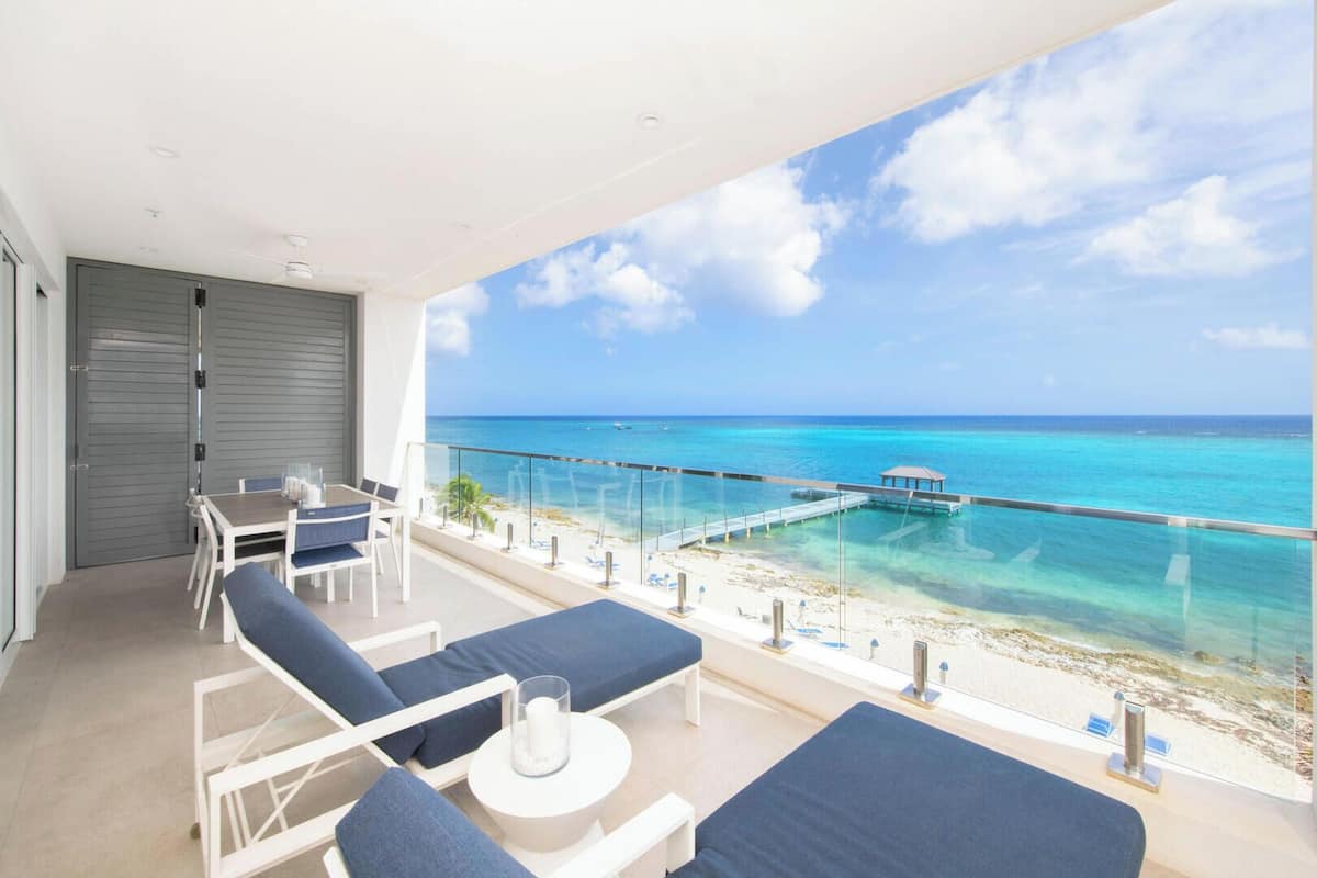 A balcony with a view of the ocean, a dining table, and lounge chairs.