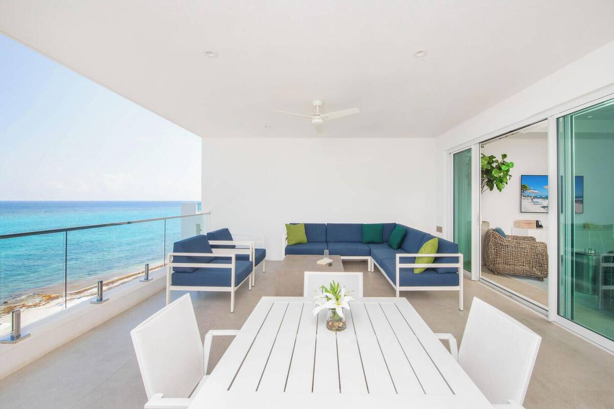A balcony with a white table and chairs, a blue sofa, and a view of the ocean.