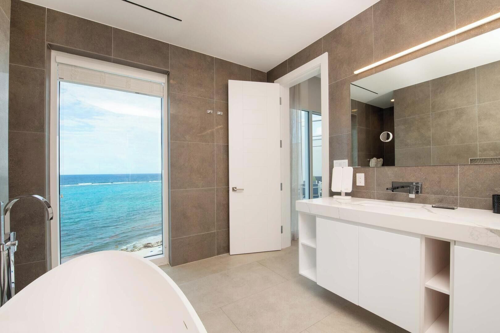 A modern bathroom with a bathtub, a large mirror, and a view of the ocean.