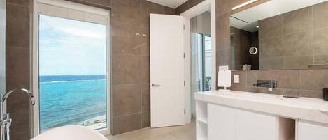A modern bathroom with a bathtub, a large mirror, and a view of the ocean.
