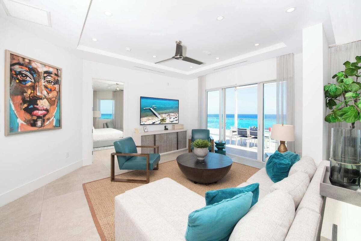 A modern living room with a large TV, comfortable seating, and a view of the ocean.