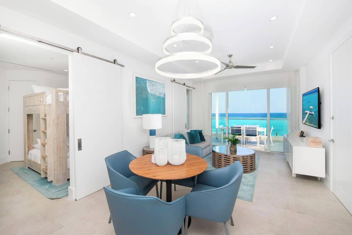 A modern hotel room with a balcony, a round wooden dining table, and a ceiling fan.