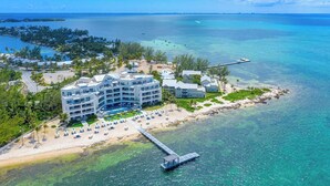Un hôtel situé sur la côte, composé de plusieurs bâtiments, avec une plage équipée de transats et une jetée qui s’avance dans l’eau.
