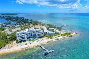 Un hôtel situé sur la côte, composé de plusieurs bâtiments, avec une plage équipée de transats et une jetée qui s’avance dans l’eau.