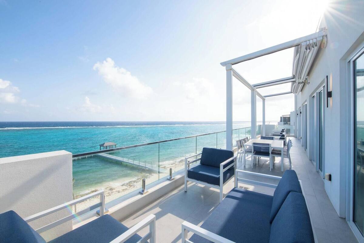 A balcony with a view of the ocean, a glass railing, and outdoor seating.