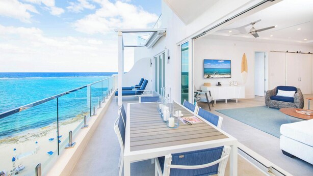 Un balcon avec vue sur l’océan, un coin repas avec une table et des chaises, et un espace de vie avec un canapé et un téléviseur.