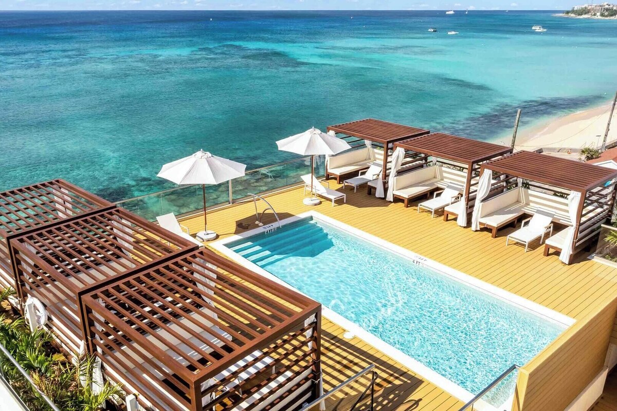 Ein Poolbereich mit Liegestühlen und Sonnenschirmen mit Blick auf einen Strand und das Meer.