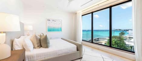 A bedroom with a large window, a bed, a ceiling fan, and a nightstand.