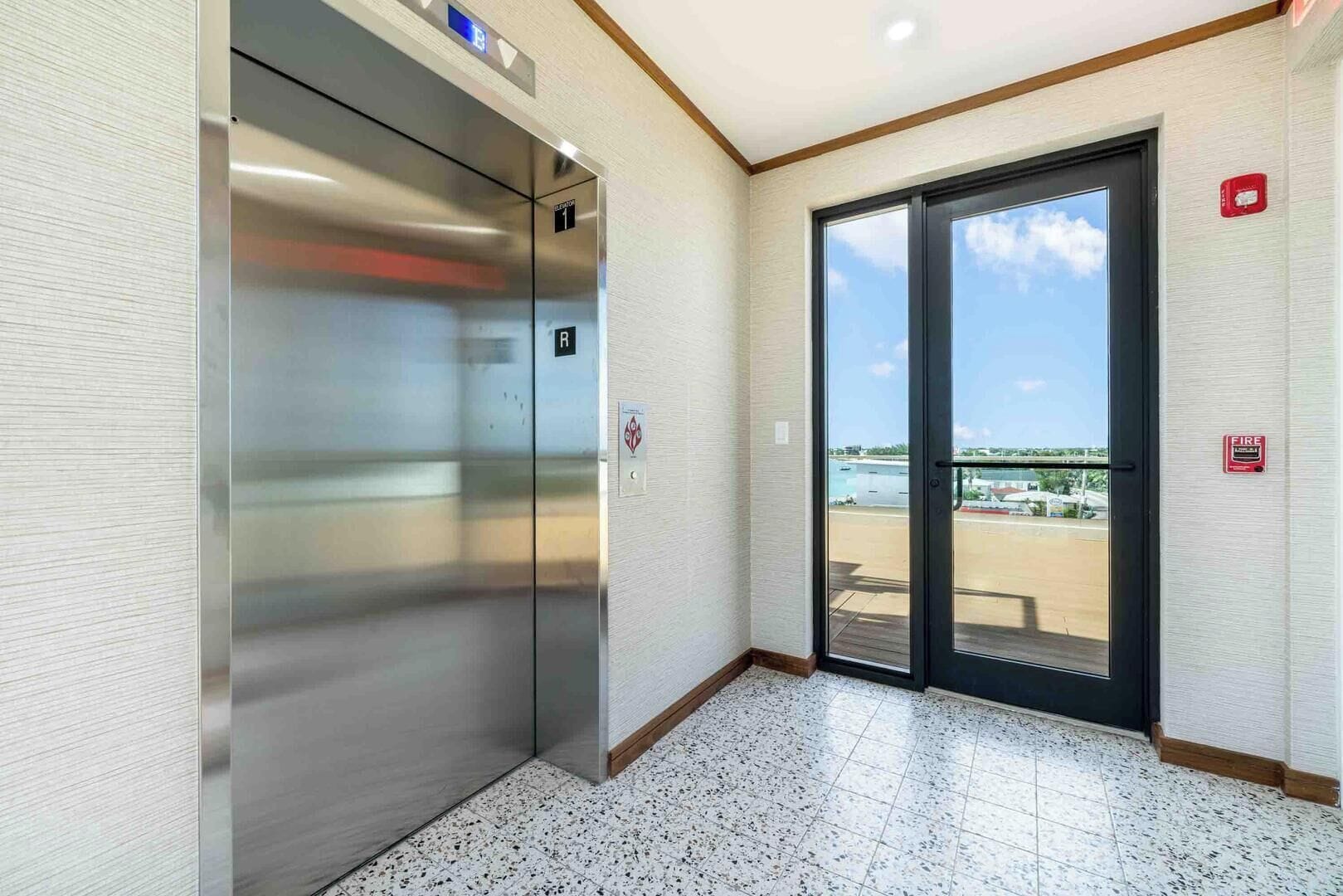 Ascensor con pantalla digital, detector de incendios y puerta que da a un balcón con vistas al agua.