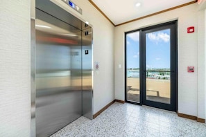 Ascensor con pantalla digital, detector de incendios y puerta que da a un balcón con vistas al agua.