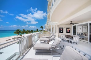 A balcony with a view of the beach and ocean, furnished with lounge chairs and a dining table. - The Beachcomber (Seven Mile Beach)