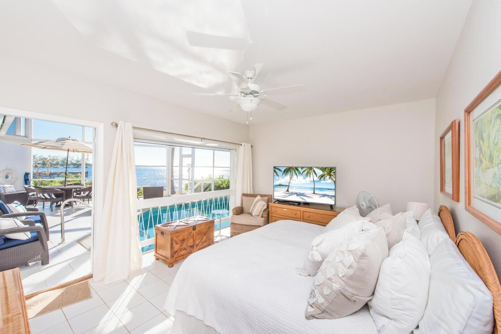A hotel room with a large bed, a TV, a balcony with a pool, and a view of the sea.