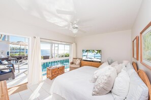 A hotel room with a large bed, a TV, a balcony with a pool, and a view of the sea. - Pools of the Kai (North Side)