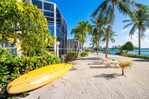 A beachside hotel with a yellow surfboard, palm trees, and a clear view of the ocean. - Pools of the Kai (North Side)