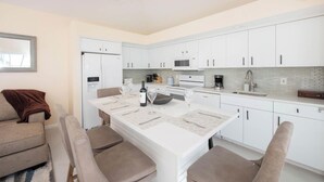 A modern kitchen with white cabinets, a dining table with chairs, and a ceiling fan. - Pools of the Kai (North Side)