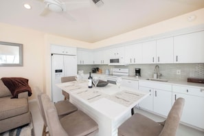 A modern kitchen with white cabinets, a dining table with chairs, and a ceiling fan. - Pools of the Kai (North Side)