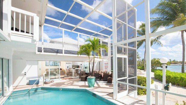 A modern pool area with glass walls, a pool, and outdoor furniture. - Pools of the Kai (North Side)