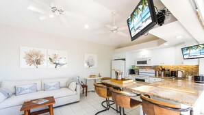 A modern kitchen with a central island, bar stools, and a flat-screen TV. - Pools of the Kai (North Side)