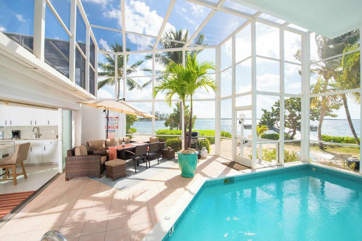 A spacious indoor pool area with a view of the sea, a dining area with outdoor seating, and a kitchen.