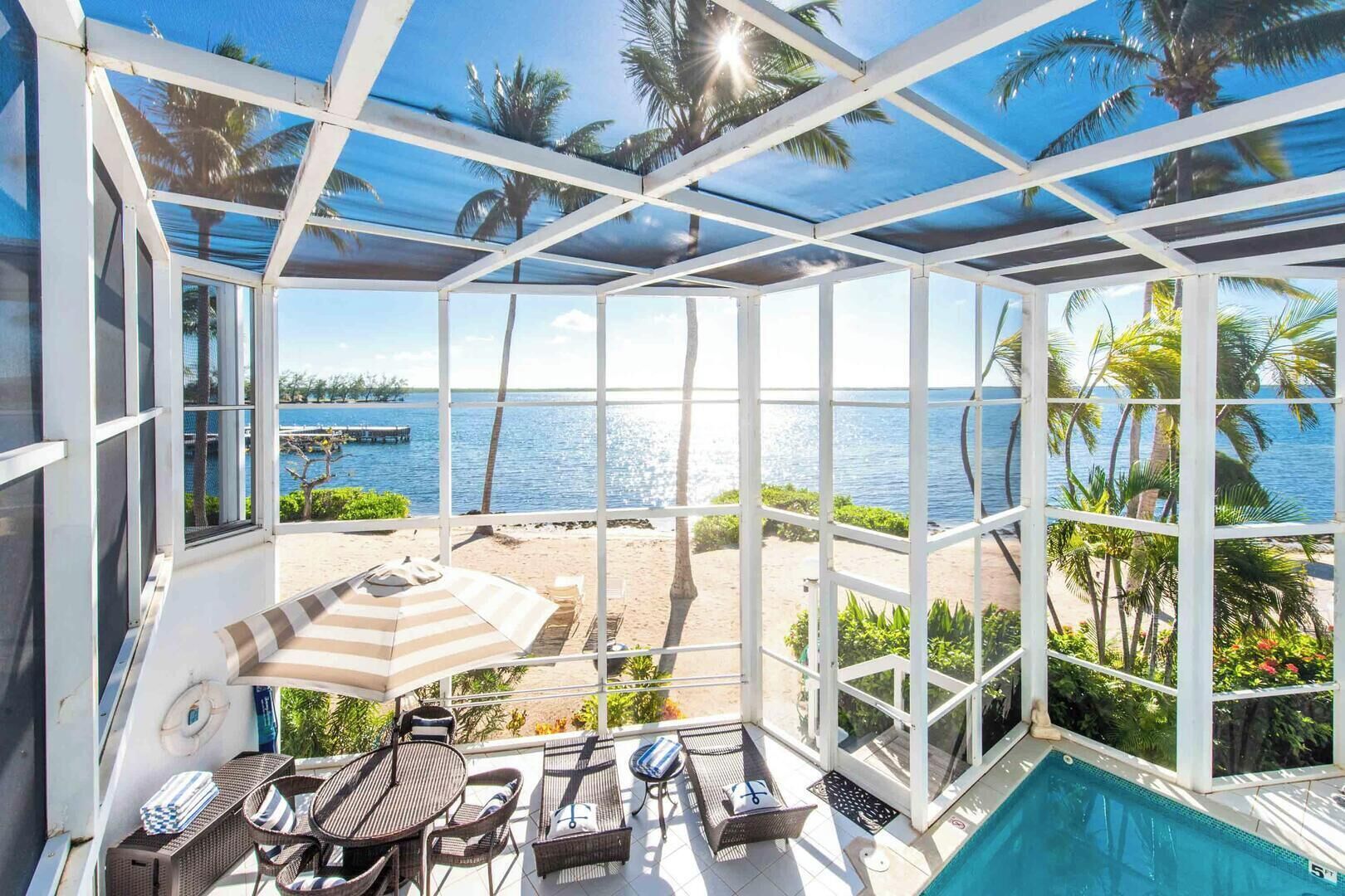 A sunroom with a view of a beach and a pool.