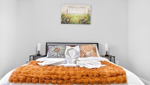 A neatly made bed with a fluffy orange blanket, white linens, and decorative pillows. There is a framed inspirational quote above the bed. - Charming 1-bedroom apartment with AC in vibrant Durham (Durham)