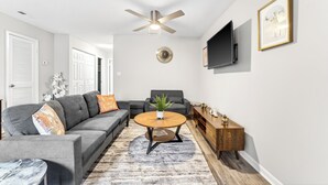 A living room with a gray sectional sofa, a round coffee table, a wooden sideboard, a ceiling fan, a clock, and a framed picture on the wall. - Charming 1-bedroom apartment with AC in vibrant Durham (Durham)