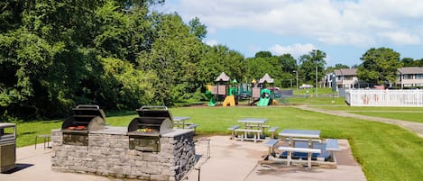 A park with a barbecue area, picnic tables, and playground equipment.