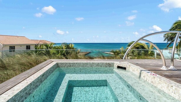 Ein Schwimmbad mit klarem Wasser, einer Holzterrasse und Blick auf das Meer und den Strand.