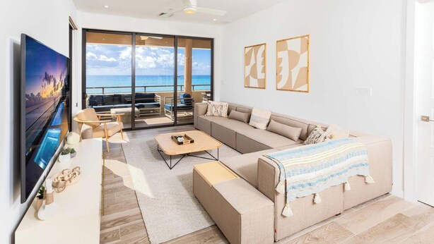 Un salon moderne doté d’un grand téléviseur, d’un canapé, d’une table basse et d’un balcon offrant une vue sur la mer.