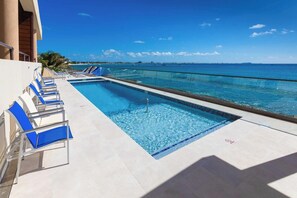 A pool with clear blue water, a glass barrier, and a view of the ocean. - SeaDreams Boutique Condos (West Bay)