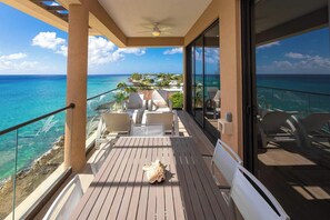 A balcony with a wooden floor, white chairs, and a small table. - SeaDreams Boutique Condos (West Bay)
