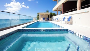 Une piscine à l’eau cristalline, une balustrade en verre et des chaises longues.