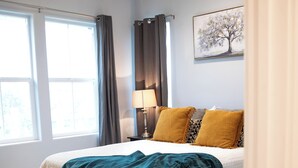 Een slaapkamer met een bed, een raam, een lamp en een schilderij aan de muur.