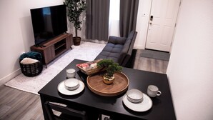 Een eethoek met een tafel voor vier personen, een televisie, een bank en een potplant.