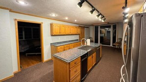 Eine Küche mit Holzausstattung, Granit Arbeitsplatten, einem Edelstahl-Kühlschrank und Einbauleuchten.
