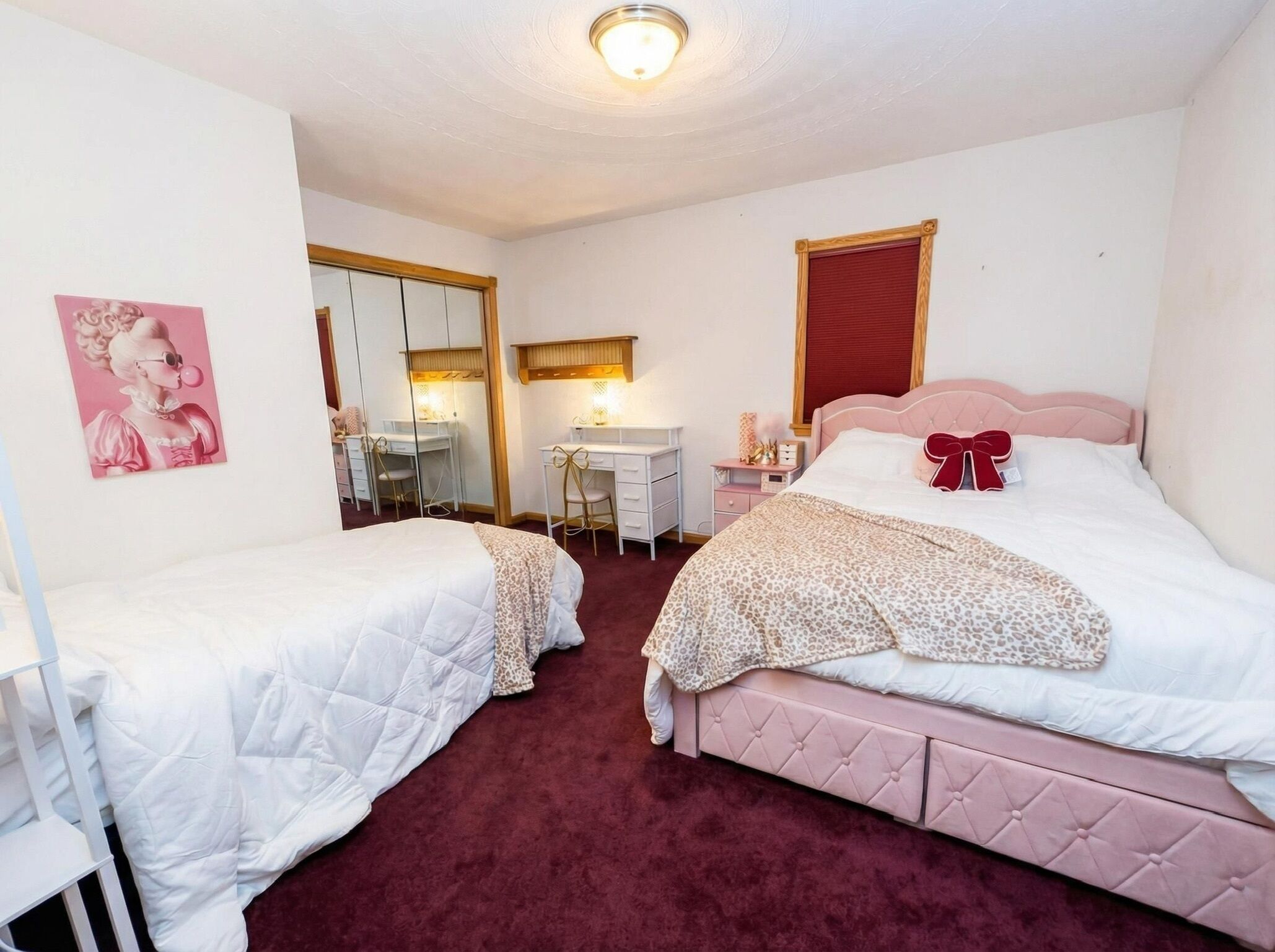 A bedroom with two beds, a desk, and a mirror.