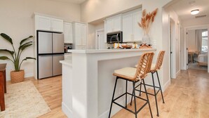 A modern kitchen with white cabinetry, a central island with bar stools, and a refrigerator. - Modern Japandi Home with Fire-Pit Evenings and Fast Internet (Meridian)