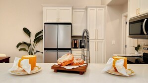 A modern kitchen with white cabinetry, a stainless steel refrigerator, and a microwave. There are two plates with bread on a wooden board. - Modern Japandi Home with Fire-Pit Evenings and Fast Internet (Meridian)