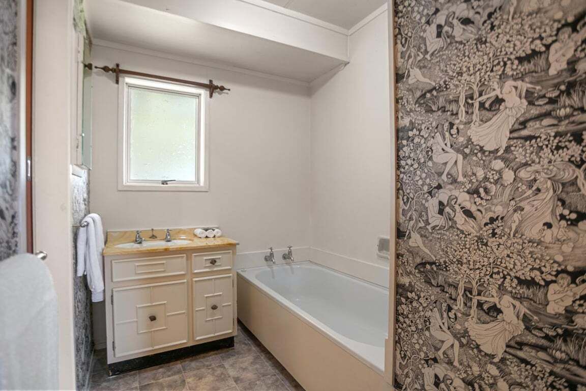 Un bagno con una vasca, un mobile vanitario con cassetti, una finestra e una parete con motivo floreale.