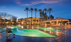 A swimming pool with lounge chairs and umbrellas, surrounded by palm trees and a building with arched windows. - Wyndham 1-Bedroom Studio in a Premier Resort with Full Amenities (Phoenix)